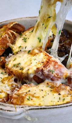 a close up of food in a bowl with cheese being lifted from the side by a spatula