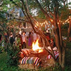 a group of people gathered around a fire pit with lights strung from the tree branches