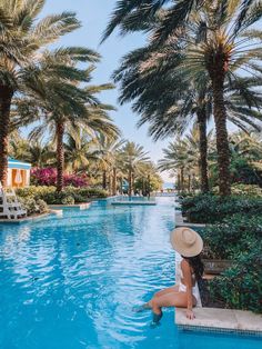 a woman sitting on the edge of a pool surrounded by palm trees