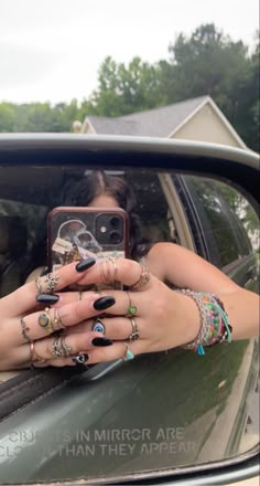 a woman taking a selfie in her car mirror with rings on her fingers and nails