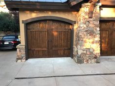 two wooden garage doors in front of a stone building with a car parked on the driveway