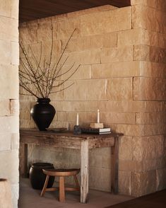 a wooden table sitting next to a black vase on top of a stone wall in a living room