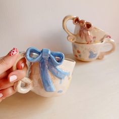 a hand holding a tea cup with a bow on it and another mug in the background