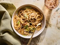 a white bowl filled with pasta and mushrooms on top of a table next to a drink