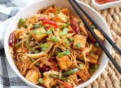 a white bowl filled with noodles and vegetables next to chopsticks on a table