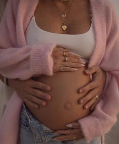 a pregnant woman with her hands on her belly wearing gold rings and a pink cardigan