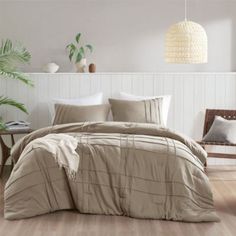 a bed with beige sheets and pillows in a white room next to a wooden chair