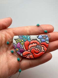 a hand holding a piece of jewelry with flowers on it