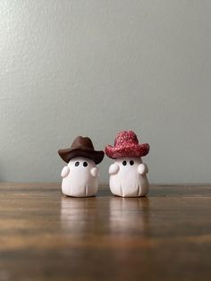 two small white figurines wearing hats on top of a wooden table