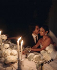 a bride and groom sitting at a table with candles