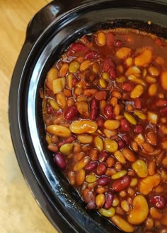 a crock pot filled with beans and other food sitting on top of a wooden table