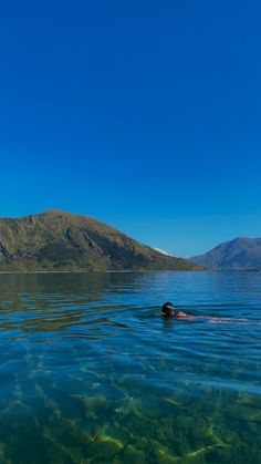 a person swimming in the water with mountains in the background and blue sky above them