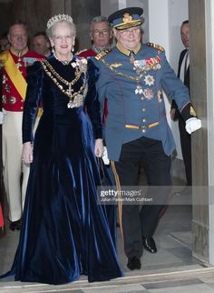 an older man and woman in formal dress walking down a hall together with other people