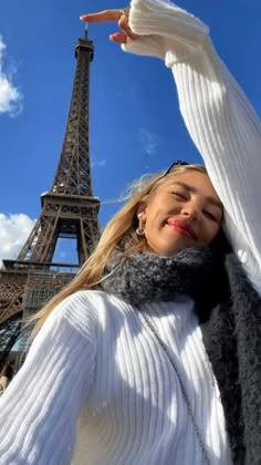 a woman standing in front of the eiffel tower with her hands up to her head