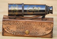 an old fashioned brass telescope sitting on top of a wooden box with writing on it