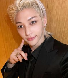 a woman with blonde hair wearing a black suit posing for a photo in front of a wooden wall