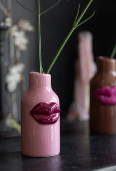 three vases with lipstick painted on them and flowers in the middle one is pink