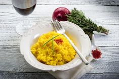 a white bowl filled with yellow rice next to a glass of wine and an onion sprig