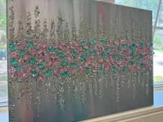 a painting with pink, green and silver flowers on it in front of a window