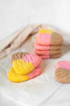 three cookies with pink, yellow and brown frosting on them sitting on wax paper