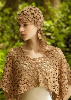 a woman wearing a brown crochet shawl in the woods with her hands on her hips