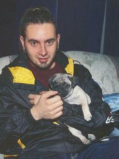 a man sitting on a couch holding a small pug dog in it's lap