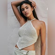 a woman posing in front of a white wall with her arms behind her head and wearing a crop top