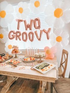 two groovy balloons are hanging above a table with desserts and snacks on it