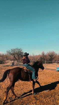 a man riding on the back of a brown horse in a dirt field next to a fence