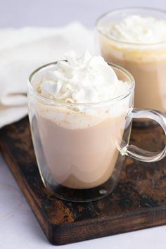 two mugs filled with whipped cream on top of a wooden tray