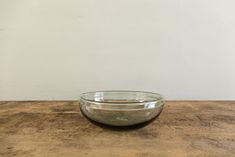 a glass bowl sitting on top of a wooden table next to a white wall in the background