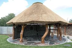 a thatched roof gazebo in a garden with stone walkways and grass walls