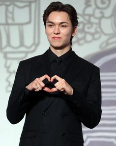 a man in a black suit making a heart with his hands while standing on stage