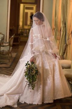 a woman in a white wedding dress and veil holding a flower bouquet on her left hand