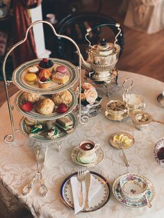 a table topped with plates and cups filled with pastries next to a tea kettle