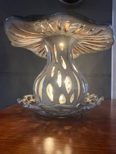 a glass candle holder on a wooden table with light coming from the top and bottom