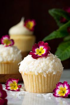 two cupcakes with white frosting and pink flowers on top are sitting next to each other