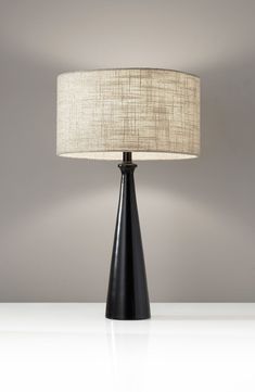 a black table lamp with a white shade on the base and a grey wall behind it