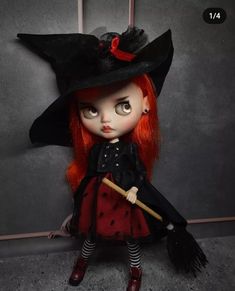 a doll with red hair wearing a black witches hat and dress, holding a broom