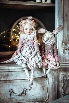 two dolls sitting on top of a dresser next to each other in front of a mirror