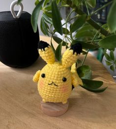 a small crocheted pikachu sitting on top of a wooden table next to a potted plant