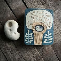 a wooden plaque with an image of a tree in the center and a white vase next to it