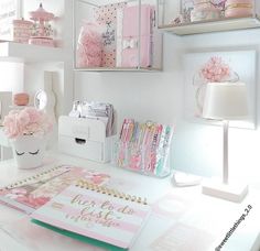 a white desk topped with lots of books and pink flowers next to a lamp on top of a table