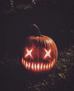 a carved pumpkin sitting in the grass with its eyes glowing orange and white, which are shaped like stars