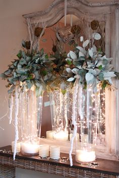 candles and flowers are sitting on a mantle in front of a mirror with greenery