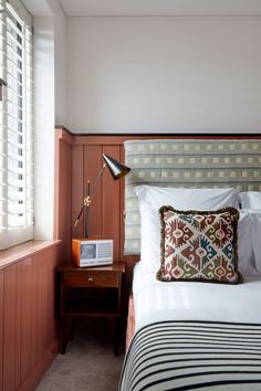 a neatly made bed in a bedroom with wood paneling and striped pillows on the headboard