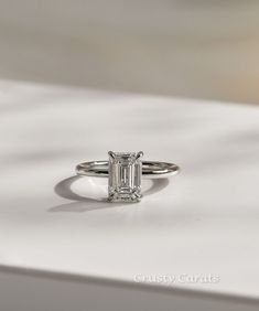 an emerald cut diamond ring sitting on top of a white surface