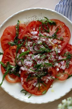 a white plate topped with sliced tomatoes and herbs