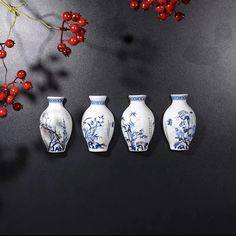 three white vases sitting next to each other with red berries on the branches behind them