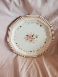 a white plate with pink flowers on it sitting on a bed covered by a sheet